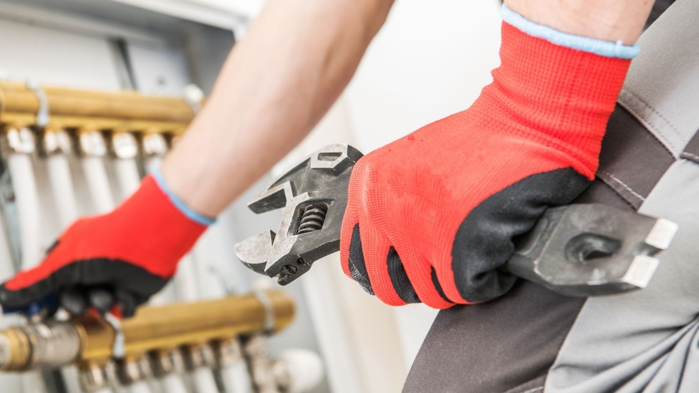 Nahaufnahme von Handschuhen, die einen verstellbaren Schraubenschlüssel an Rohrleitungen halten