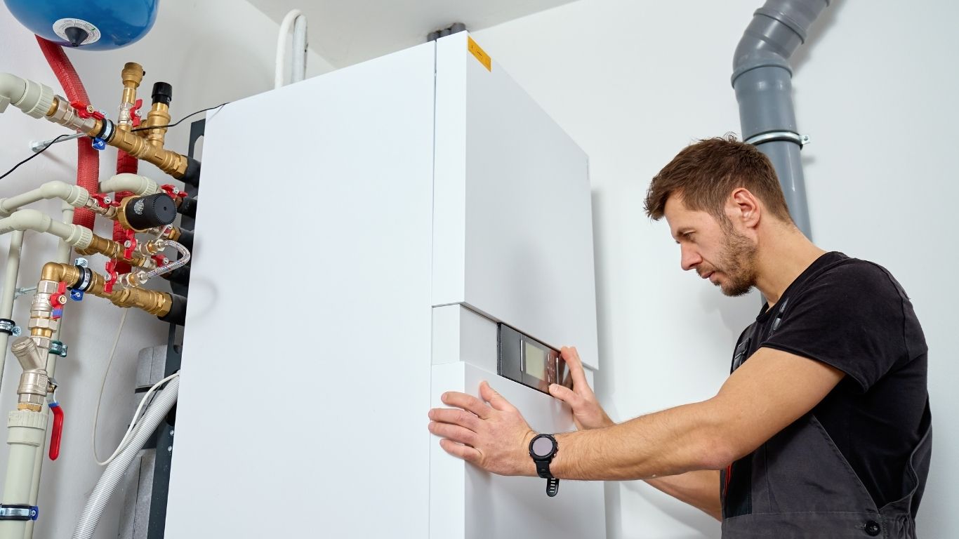 Installateur prüft eine Heizungsanlage mit großem weißem Wärmeerzeuger und sichtbaren Rohrleitungen
