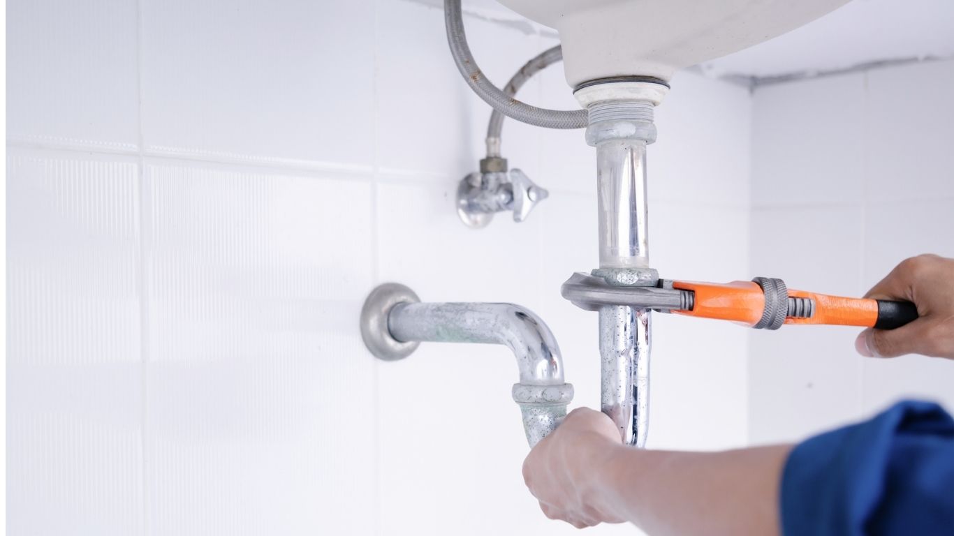 Handwerker repariert unter einem Waschbecken das Abflussrohr mit einer Rohrzange