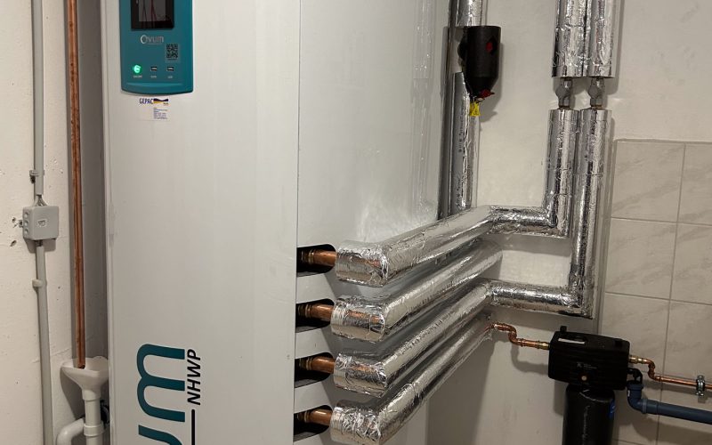 Großer weißer Wärmespeicher in einem Technikraum mit isolierten Rohren und Anschlüssen an der Wand