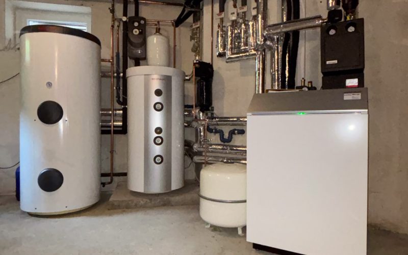 Heizungsraum mit mehreren Warmwasserspeichern, Rohrleitungen und einem großen weißen Wärmepumpengerät